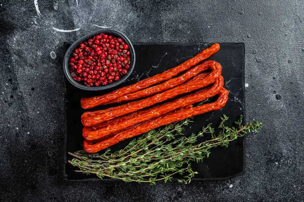 Smoked kabanos sausages with herbs on marble board. Black background. Top view.