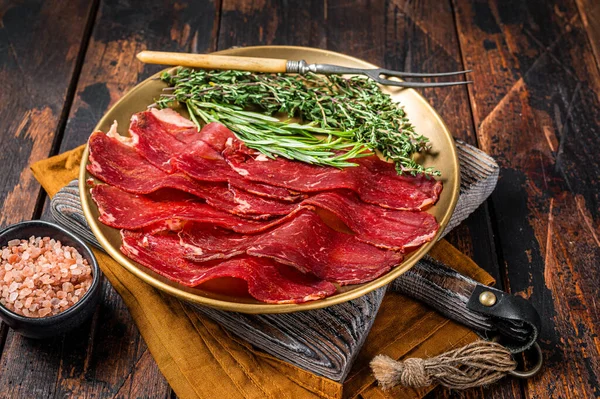 Basturma, sliced dried beef meat, meat Jerky in steel plate with herbs and spices. Wooden background. Top view.