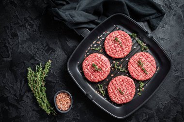 Raw Ground beef meat Burger steak cutlets in grill skillet ready for cooking. Black background. Top view.