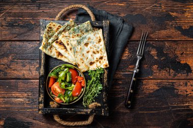 Baked Gozleme flatbread with greens in a box with vegetable salad. Wooden background. Top view.