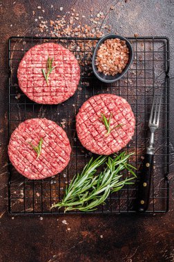 Raw burger cutlet from beef meat with spices and rosemary ready for cooking. Dark background. Top view.