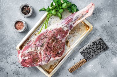 Marinated whole mutton leg, raw lamb meat with thyme, spices and olive oil. Gray background. Top view.