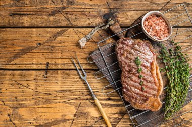 Grilled striploin or New York beef meat steak cooked on BBQ. Wooden background. Top view. Copy space.
