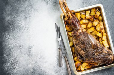 Roast lamb mutton leg with potatoes and rosemary in baking dish. White background. Top view. Copy space.