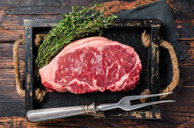 Prime raw new york beef meat steak with herbs ready for cooking. Wooden background. Top view.