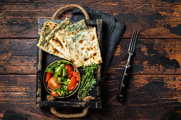 Baked Gozleme flatbread with greens in a box with vegetable salad. Wooden background. Top view.