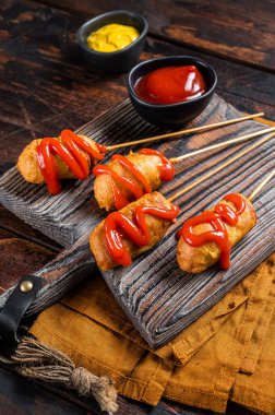 Mini Deep fried corn dogs with mustard and ketchup on wooden board. Wooden background. Top view.