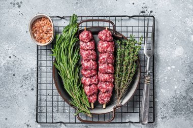 Raw Turkish Urfa kebab decorated with herbs, spices and meat fork. Gray background. Top view.