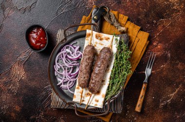 Turkish Adana Kebab from mince lamb beef meat on Skewer with flatbread and onion. Dark background. Top view.