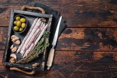 Meat Charcuterie Fuet salami sausages with olives and herbs. Wooden background. Top view. Copy space.