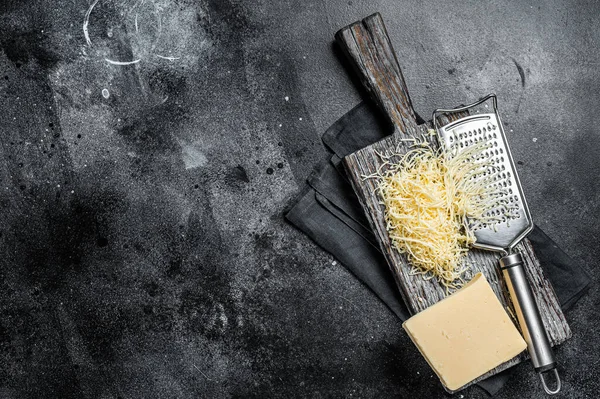 Grated cheese for cooking on a cutting board . Black background. Top view. copy space.