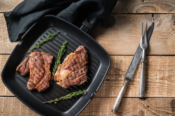 Grilled Chuck eye Roll beef steaks with herbs on grill skillet. Wooden background. Top view.