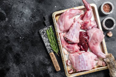 Çiğ yaban tavşanı, bacaklar, çelik tepside taze et ve bitki. Siyah arka plan. Üst Manzara. Boşluğu kopyala.