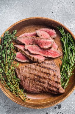 Grilled sliced Skirt Steak on a plate with herbs. Gray background. Top view.