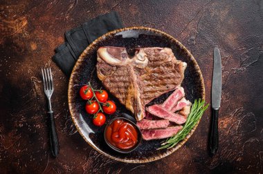 Biftekli ızgara biftek, domatesli bir tabakta pişmiş kemik. Karanlık arka plan. Üst görünüm.