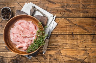 Sliced raw chicken, turkey breast meat in a wooden plate with thyme. Wooden background. Top view. Copy space.