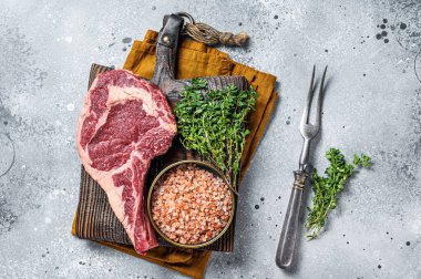 Raw uncooked black angus beef cowboy or rib eye steak. Gray background. Top view.