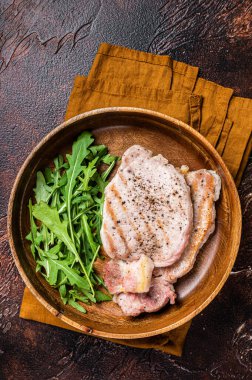 Roasted pork chop steaks or cutlets with arugula salad. Dark background. Top view.