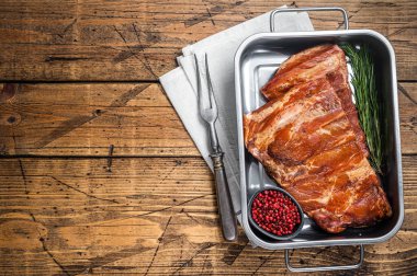 American Smoked Pork spare Ribs in steel tray with herbs. Wooden background. Top view. Copy space.