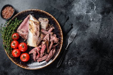 Smoked and grilled beef short ribs in rustic plate with herbs. Black background. Top view. Copy space.