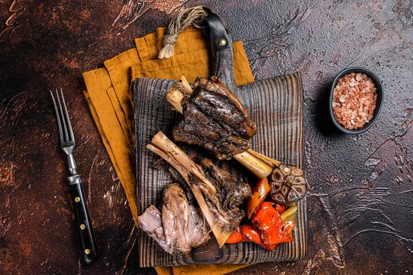 Traditionally slow cooked Leg of Lamb or Lamb Shank with vegetables on a cutting board. Dark background. Top view.