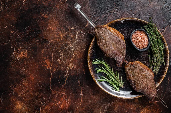 Brazilian BBQ - grilled dry aged picanha beef steak with herbs. Dark background. Top view. Copy space.