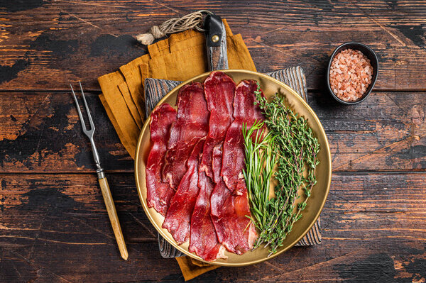 Basturma, sliced dried beef meat, meat Jerky in steel plate with herbs and spices. Wooden background. Top view.