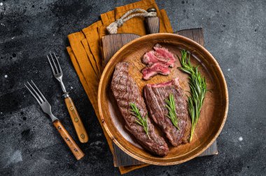 Fried sirloin flap or flank beef steak with herbs in a wooden plate. Black background. Top view.