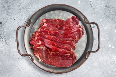 Sliced basturma, cured beef meat in steel tray. Gray background. Top view.