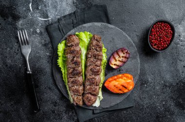 Grilled Urfa kebab with tomato, salad and onion. Black background. Top view.