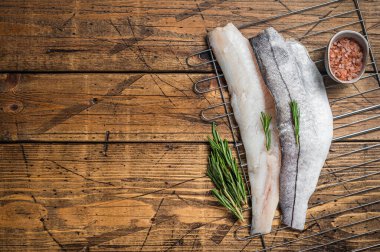 Raw fish fillets on grill with rosemary and herbs. Wooden background. Top view. Copy space.