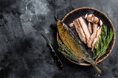 Hot Smoked herring fish fillet on rustic plate with thyme and rosemary. Black background. Top view. Copy space.