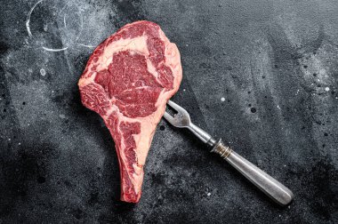 Raw cowboy steak, rib eye steak with bone, beef marbled meat on butcher cutting board. Black background. Top view. Copy space.