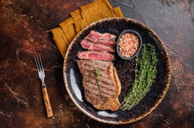 BBQ roast sliced New York beef steak on a plate with thyme and salt. Dark background. Top view.