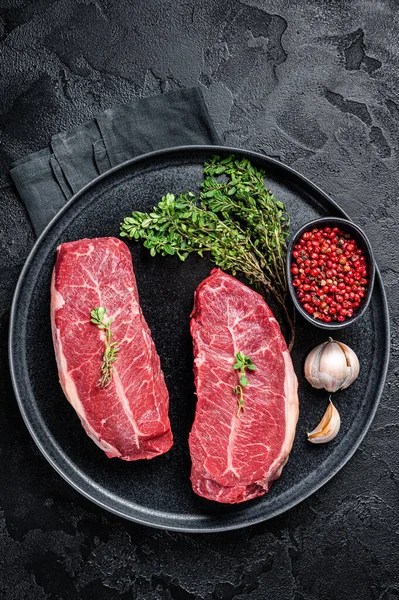 Dry aged Raw top blade flat Iron beef meat steaks. Black background. Top View.