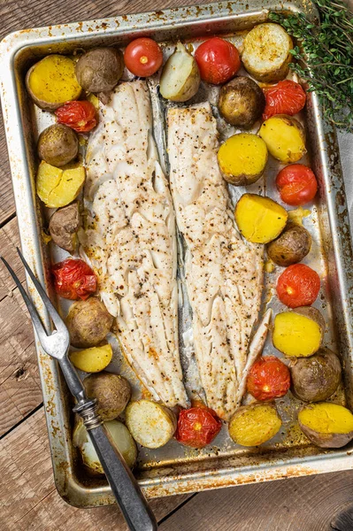 Hake fish fillet, roasted fish meat with tomato and potato. Wooden background. Top view.
