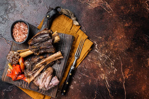 Traditionally slow cooked Leg of Lamb or Lamb Shank with vegetables on a cutting board. Dark background. Top view. Copy space.
