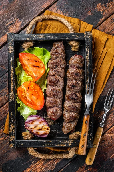 Traditional middle east kefta or kofta kebab, ground beef and lamb meat grilled on skewers served with tomato, salad and onion. Wooden background. Top view.