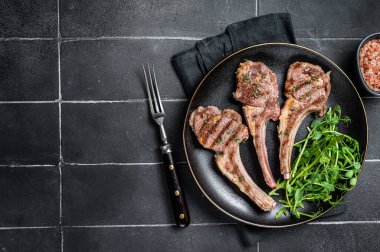 Roasted lamb meat cutlets, mutton chops with garnish. Black background. Top view. Copy space.