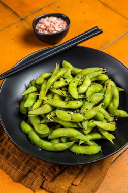 Boiled Edamame Soy Beans with sea salt and sesame seeds. Orange background. Top view.