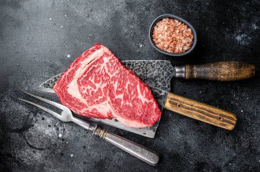 Butcher table with wagyu Rib Eye steak, raw beef meat. Black background. Top view.