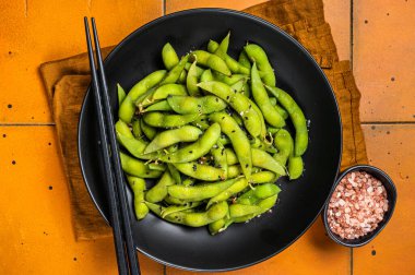 Boiled Edamame Soy Beans with sea salt and sesame seeds. Orange background. Top view.