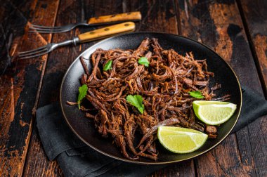 Carnitas in a plate with celery and lime wedges. Wooden background. Top view.