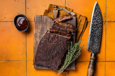 Smoked Barbecue Beef Brisket with Sauce on wooden board. Orange background. Top view.