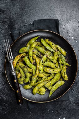 Stir-fried green Edamame Soy Beans with sea salt and sesame seeds in a plate. Black background. Top view.