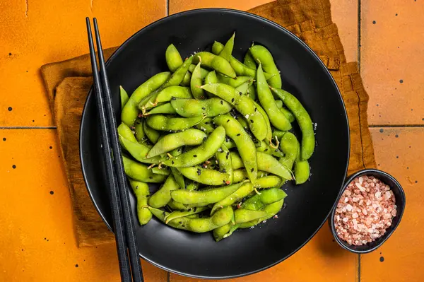 Boiled Edamame Soy Beans with sea salt and sesame seeds. Orange background. Top view.