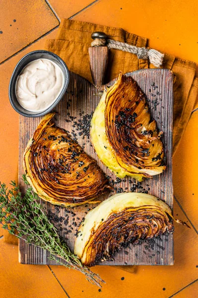 Roasted vegan cabbage steaks with herbs on wooden board. Orange background. Top view.
