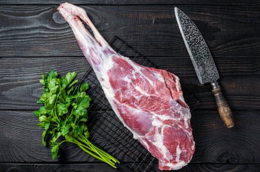 Fresh Raw whole lamb mutton leg thigh on kitchen table with herbs. Black Wooden background. Top view.