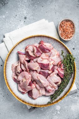 Raw chicken stomachs offals in a plate with herbs. Gray background. Top view.