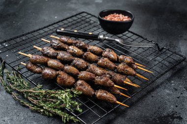 Grilled shish kebab with chicken hearts on a grill. Black background. Top view.